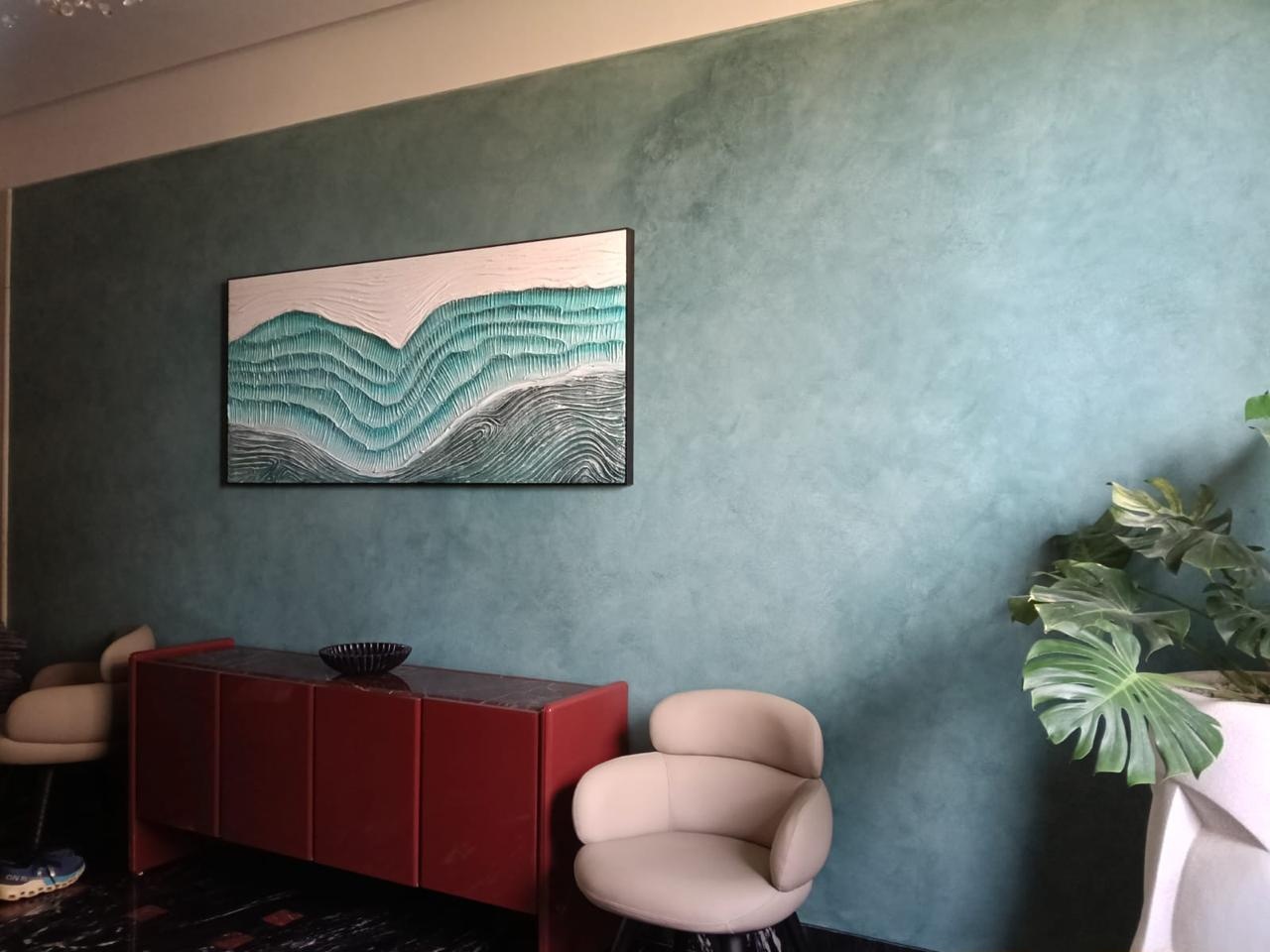 Teal textured feature wall with wave artwork, red cabinet and cream chairs